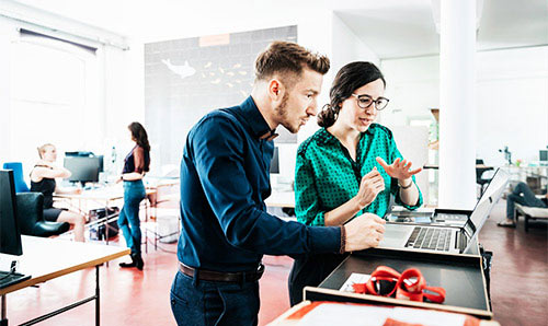 Two office workers discussing the content on a laptop in an office environment