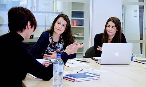 Three colleagues sit around a table having a discussion.