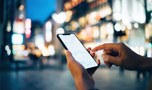 A person on a smartphone with buildings and bright lights in the background